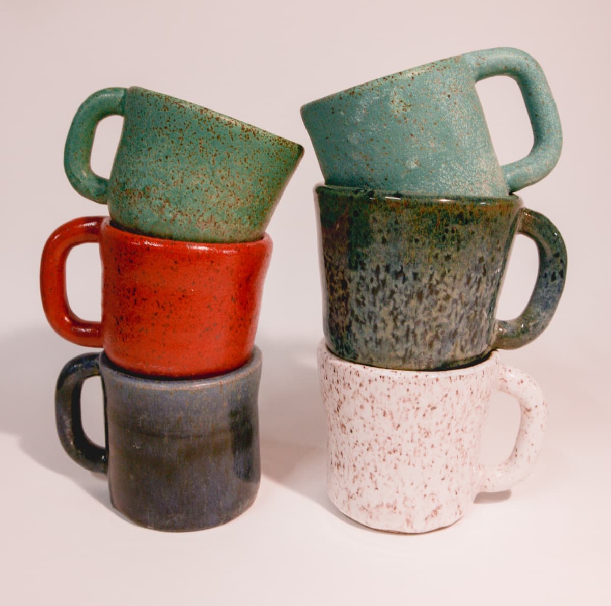A stack of six hand-glazed Wry Pottery mugs in assorted colors